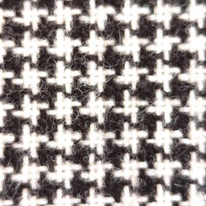 May include: Close-up of a black and white houndstooth pattern. The repeating design features white crosses on a dark background, creating a textured appearance. The fabric has a slightly fuzzy texture.