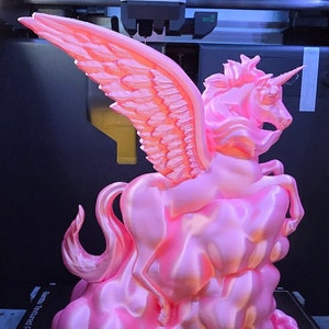 May include: A pink 3D-printed sculpture of a winged unicorn, also known as a pegasus, atop a cloud-like base. The sculpture has a glossy finish and is set against a dark background. The wings are detailed with individual feathers.