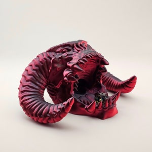 May include: A red, 3D printed dragon head dice holder with a single die inside. The dragon has sharp teeth and horns.