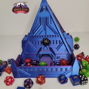 May include: A blue pyramid-shaped dice tower with a detailed, futuristic design. The tower has a central opening and is surrounded by various colourful polyhedral dice. The Fates End logo is visible.