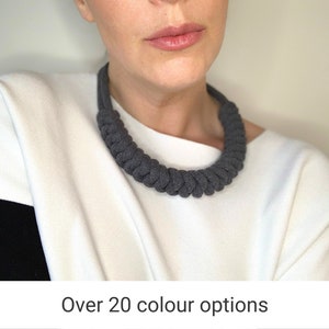 May include: A woman wearing a white shirt with a black stripe on the sleeve is wearing a grey knotted rope necklace. The necklace is thick and has a simple design.  Over 20 colour options are available.