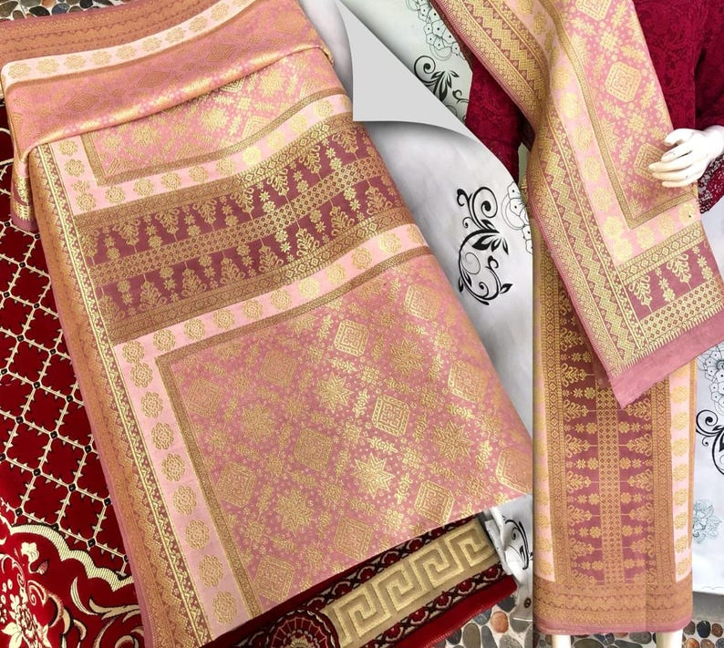 Pu&ograve; includere: Tessuto rosa e oro a fantasia con disegni intricati. Il tessuto presenta un motivo geometrico ripetuto e un bordo con un motivo floreale dettagliato. La tavolozza dei colori comprende sfumature di rosa, oro e bordeaux. Il tessuto &egrave; probabilmente utilizzato per scopi decorativi.