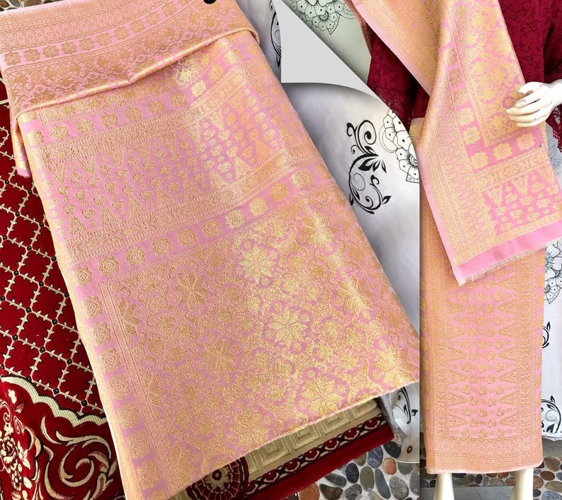 Pu&ograve; includere: Tessuto rosa e oro con intricati motivi floreali e geometrici. Il tessuto &egrave; piegato, rivelando il design dettagliato. Il tessuto &egrave; probabilmente un tessuto decorativo o un capo d'abbigliamento.