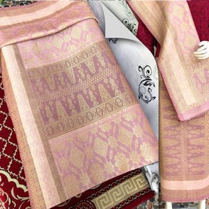 Pu&ograve; includere: Tessuto rosa e oro con motivi intricati. Il tessuto &egrave; drappeggiato per mostrare la sua consistenza e i dettagli. La tavolozza dei colori include sfumature di rosa e oro, creando un aspetto lussuoso. Il tessuto sembra essere un tessuto, forse per abbigliamento o arredamento.