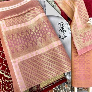 Pu&ograve; includere: Una collezione di tessuti rosa e oro con motivi intricati. I tessuti presentano disegni floreali e geometrici, con un mix di sezioni a tinta unita e fantasia. I tessuti sono probabilmente utilizzati per abbigliamento o arredamento.