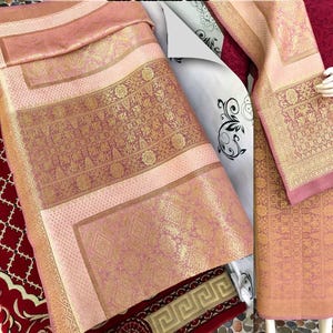 Pu&ograve; includere: Tessuto rosa e oro con motivi intricati. Il tessuto sembra essere piegato e drappeggiato, mostrando i motivi e le trame dettagliate. La tavolozza dei colori include sfumature di rosa e oro.
