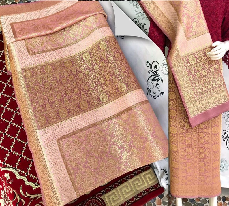 Pu&ograve; includere: Tessuto rosa e oro con motivi intricati. Il tessuto sembra essere piegato e drappeggiato, mostrando i motivi e le trame dettagliate. La tavolozza dei colori include sfumature di rosa e oro.