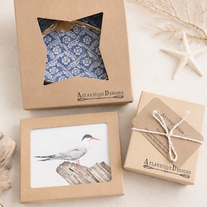 Puede incluir: Tres cajas de regalo de cart&oacute;n marr&oacute;n con el logotipo de Atlantique Designs. Una caja tiene un recorte en forma de estrella que muestra tela floral azul, otra un recorte rectangular con una ilustraci&oacute;n de un p&aacute;jaro y la tercera est&aacute; atada con cuerda blanca.