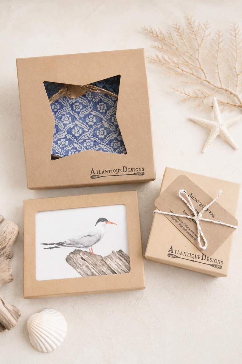 Puede incluir: Tres cajas de regalo de cart&oacute;n marr&oacute;n con el logotipo de Atlantique Designs. Una caja tiene un recorte en forma de estrella que muestra tela floral azul, otra un recorte rectangular con una ilustraci&oacute;n de un p&aacute;jaro y la tercera est&aacute; atada con cuerda blanca.