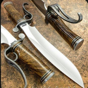 May include: A custom-made knife with a long, curved blade and a wooden handle. The handle is decorated with intricate patterns and has a metal ring at the end. The knife is resting on a brown surface.