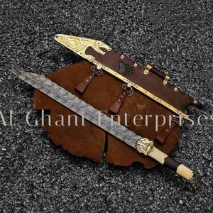 Puede incluir: Imagen detallada de una espada y su vaina. La espada tiene una hoja estampada y un mango decorativo. La vaina es de cuero marrón con detalles dorados. El texto "Al Ghani Enterprises" es visible.