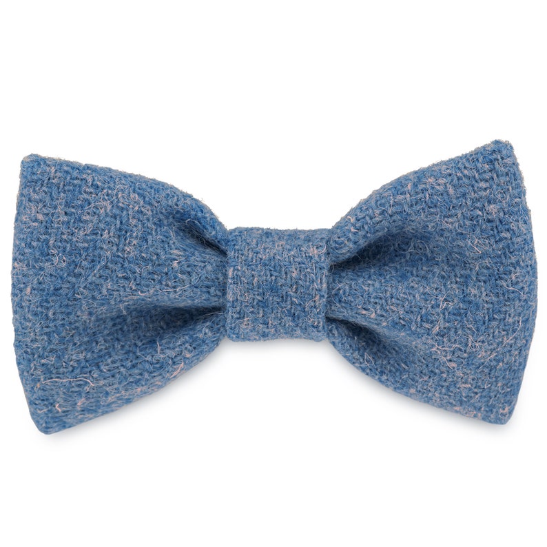 May include: A blue bow tie made of a textured fabric. The bow tie has a light pink undertone.