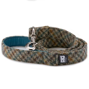 May include: A brown and green tweed dog leash with a teal leather lining and a silver clip. The leash has a black label with the text "Hemove" and a logo.