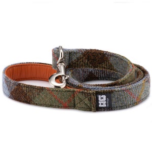 May include: A green, blue, and brown tweed dog leash with an orange leather lining and a silver clip. The leash has a brown leather patch with the text "MG Heritage" in white.