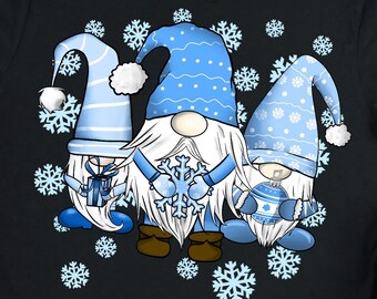 May include: A black short-sleeved t-shirt featuring a graphic of three gnomes wearing blue and white patterned hats, surrounded by light blue snowflakes. The gnomes are holding a gift, a large snowflake, and a blue ornament respectively.