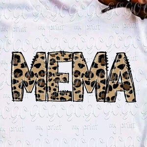 May include: A white short-sleeved t-shirt featuring the word MEMA printed in a brown and black leopard print pattern. The shirt is displayed with brown sunglasses, blue denim jeans, and brown strappy sandals arranged around the garment.