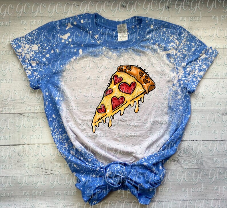 May include: A blue short-sleeve t-shirt with a bleached white center section. The graphic features a slice of pizza with melting cheese and red heart-shaped pepperoni slices. The shirt has a crew neckline and a knotted hem at the bottom.