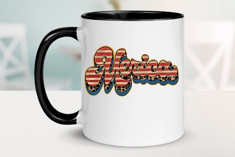 May include: White ceramic mug with a black rim and handle. The mug features a graphic of the word "Merica" in a retro font with red, white, and blue stripes and a leopard print pattern.