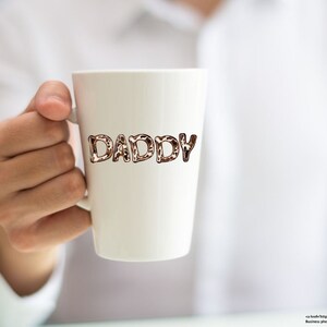 May include: White ceramic mug with the word "DADDY" written in brown and black leopard print letters.