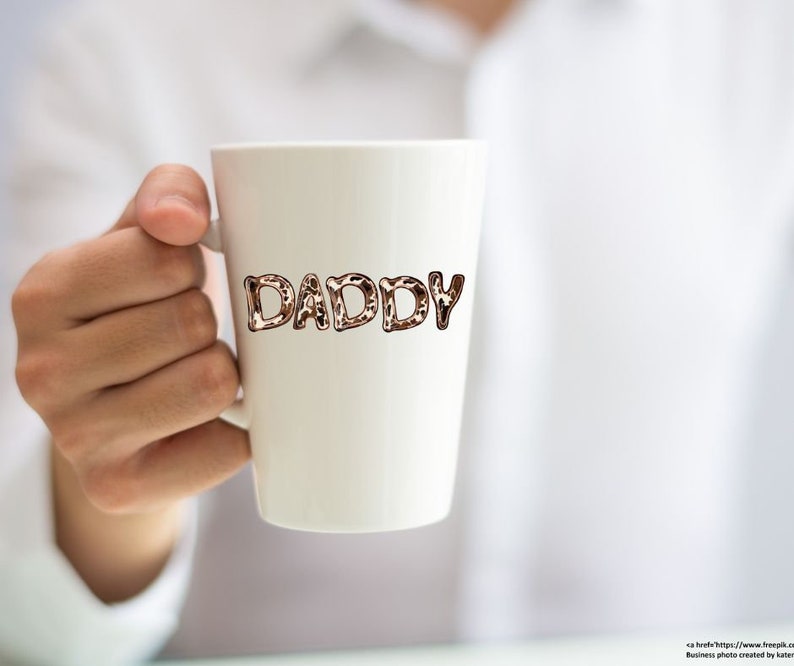 May include: White ceramic mug with the word "DADDY" written in brown and black leopard print letters.