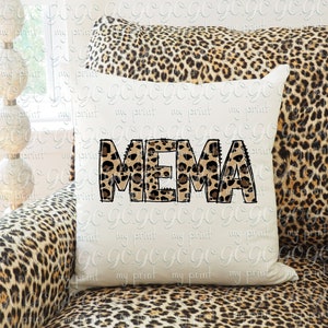 K&ouml;nnte beinhalten: Ein wei&szlig;es Kissen mit dem Wort "MEMA" in braunen und schwarzen Leopardenmuster-Buchstaben. Das Kissen liegt auf einem braunen und schwarzen Leopardenmuster-Sofa.