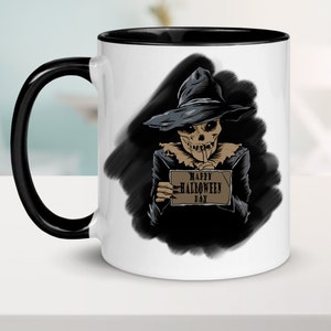 Peut inclure: Mug en c&eacute;ramique blanche avec une anse et un bord noirs. Le mug pr&eacute;sente une illustration en noir et blanc d'un squelette portant un chapeau de sorci&egrave;re et tenant une pancarte qui dit "Happy Halloween Day".