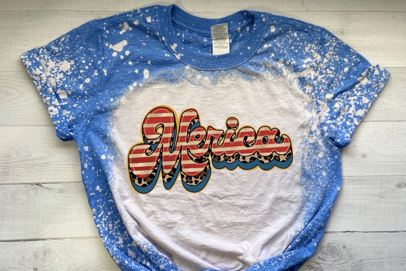 May include: A white t-shirt with a blue splatter design on the sleeves. The shirt has a red, white, and blue "Merica" graphic with a leopard print design.