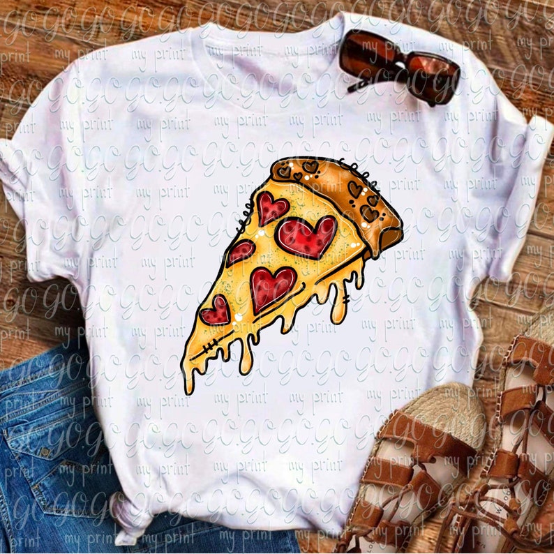 May include: A white short-sleeve t-shirt featuring a graphic of a pizza slice with melted cheese and red heart-shaped pepperoni toppings. The design includes a crust with small heart patterns. The shirt is paired with blue denim jeans and brown sandals.