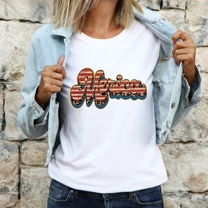 May include: White t-shirt with a red, white, and blue "Merica" graphic. The graphic is in a retro font and features a leopard print pattern.