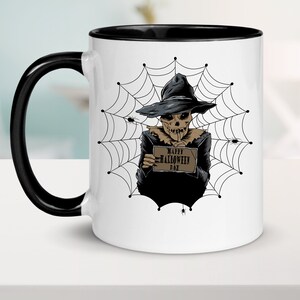 K&ouml;nnte beinhalten: Eine wei&szlig;e Keramiktasse mit schwarzem Henkel und Rand. Die Tasse zeigt eine Schwarzwei&szlig;illustration eines Skeletts, das einen Hexenhut tr&auml;gt und ein Schild mit der Aufschrift "Happy Halloween Day" vor einem Spinnennetz-Hintergrund h&auml;lt.
