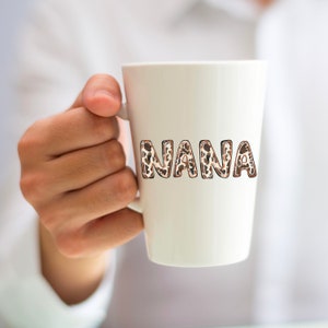 Puede incluir: Taza de cer&aacute;mica blanca con la palabra "NANA" escrita en letras marrones y beige con un estampado de leopardo.