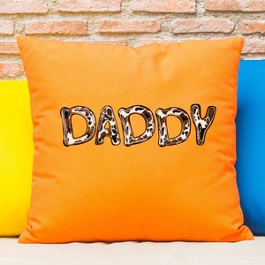 May include: Orange throw pillow with the word "DADDY" in brown and white animal print letters.