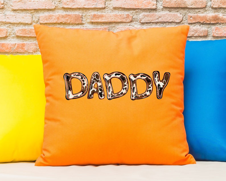 May include: Orange throw pillow with the word "DADDY" in brown and white animal print letters.