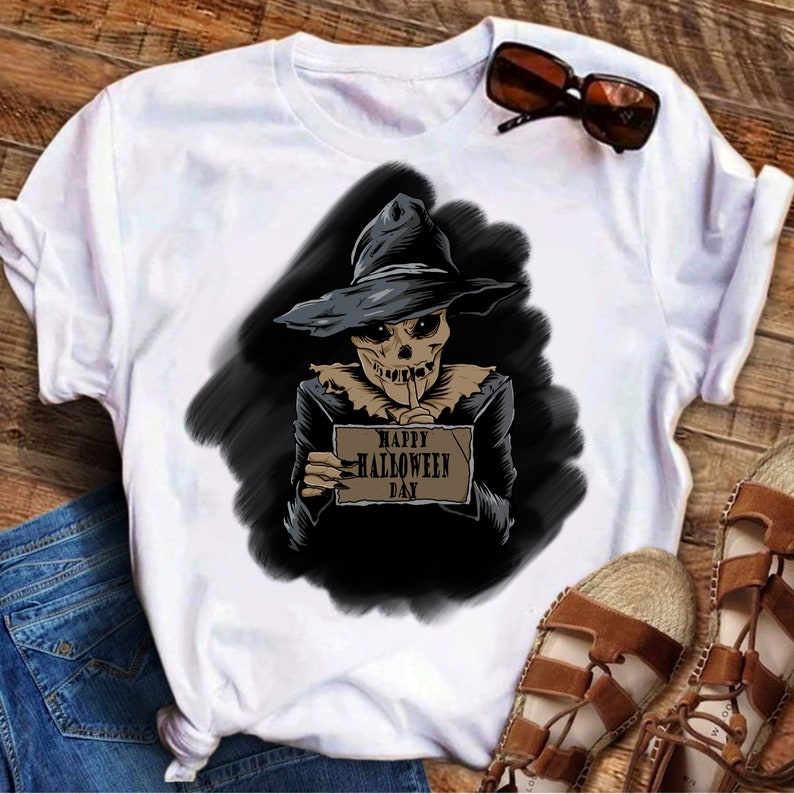 Peut inclure: T-shirt blanc avec un motif repr&eacute;sentant un squelette portant un chapeau de sorci&egrave;re et tenant une pancarte sur laquelle est &eacute;crit "Happy Halloween Day".