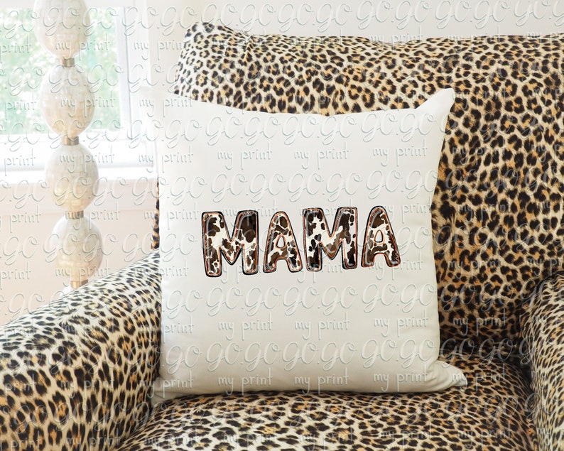 Puede incluir: Una almohada blanca con la palabra "MAMA" escrita en letras de estampado de leopardo marr&oacute;n y blanco. La almohada est&aacute; sentada en un sof&aacute; de estampado de leopardo marr&oacute;n y negro.