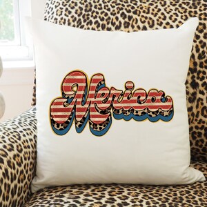 May include: White throw pillow with a red, white, and blue "Merica" graphic in a retro font. The graphic has a leopard print pattern and blue and yellow outlines.