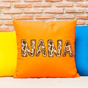 Puede incluir: Coj&iacute;n naranja con la palabra "NANA" en letras de estampado animal marr&oacute;n y blanco.