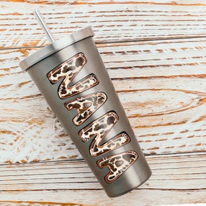 Puede incluir: Un vaso de acero inoxidable con una pajita y un dise&ntilde;o de estampado de leopardo que dice "NANA" en &eacute;l.