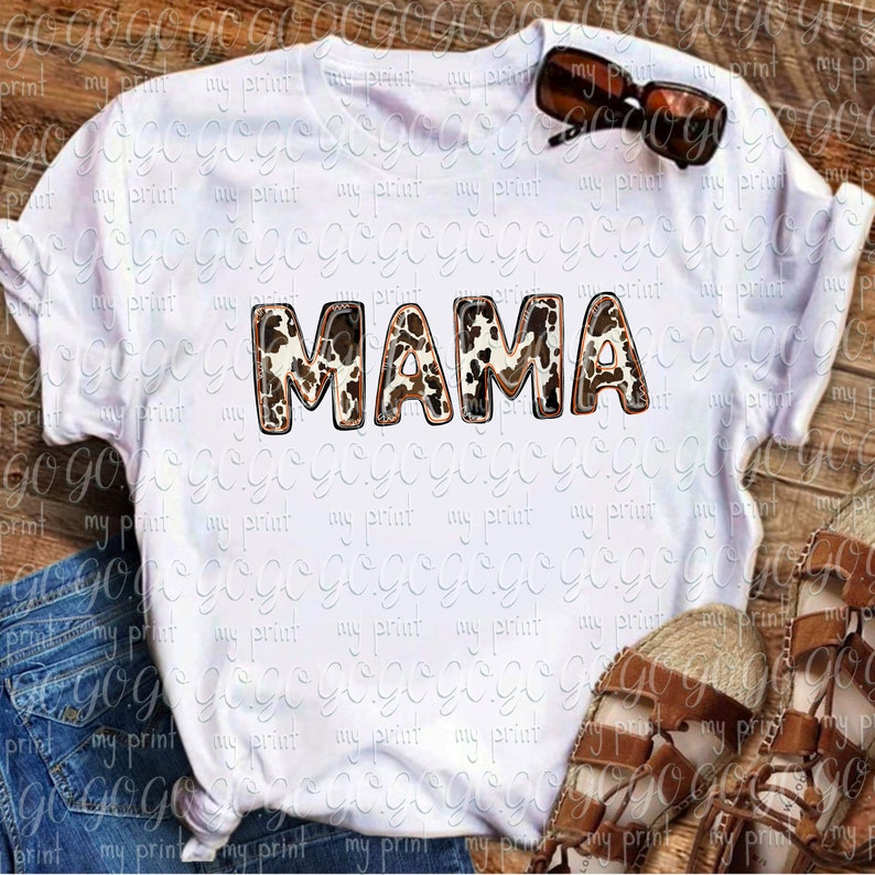 Puede incluir: Camiseta blanca con la palabra "MAMA" en letras marrones y blancas con estampado de vaca.