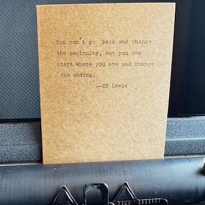 May include: A brown card with the quote "You can't go back and change the beginning, but you can start where you are and change the ending." by C.S. Lewis, displayed on a vintage typewriter.