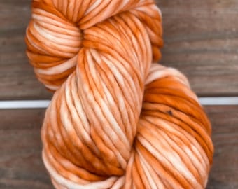 May include: A large ball of orange and cream-coloured yarn. The yarn is thick and chunky, with a soft, textured appearance. The colour is a blend of warm orange and creamy white, creating a marbled effect. Suitable for knitting or crochet projects.