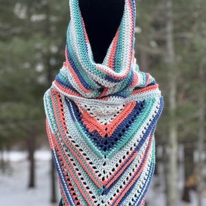 May include: A crocheted scarf with a hood in shades of blue, green, and coral. The scarf is made with a textured stitch and has a fringed edge.