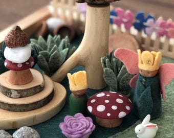 May include: A wooden playset with a pine cone tree, mushrooms, a felt rabbit, and two felt figures with crowns. The figures are standing on a green felt base with a blue felt river.