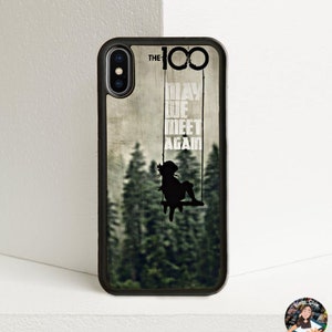 May include: A black phone case with a wood grain background and a silhouette of a girl on a swing. The text "THE 100" and "MAY WE MEET AGAIN" is printed on the case.