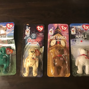 May include: Four Ty Beanie Babies from the 'Collect 'Em All '97' series. The bears are named Erin, Glory, Britannia, and Maple. Each bear is packaged in a plastic bag with a colorful background featuring a landmark from the country the bear represents. The bears are all wearing red, white, and blue clothing.