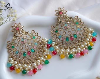 May include: A pair of gold-tone earrings with a floral design and multi-colored stones. The earrings have a dangling section with white pearls and colorful beads.
