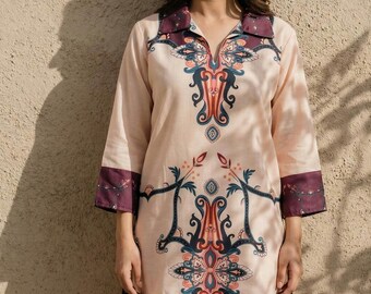 May include: A two-piece pajama set in a light peach color. The top has a collared neckline and three-quarter sleeves with dark purple cuffs. The set features a detailed, ornate design in teal, orange, and purple.