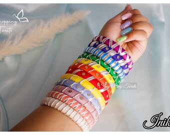 May include: A selection of vibrant bangles in a spectrum of colours, including pink, purple, blue, green, yellow, orange, and red. Each bangle features silver detailing and decorative patterns. The image includes the text "Shopping Tweets" and "Shop Ring-Tweets".