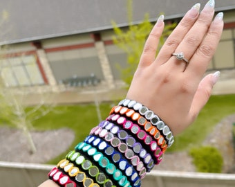 May include: A stack of colourful bracelets with mirrored accents. Each bracelet is made of a different colour fabric and features small, round mirrors.