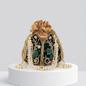 Pode incluir: Uma bolsa ornamentada, verde escuro, com acabamentos dourados e bordados florais. A bolsa apresenta um fecho de cordão e é adornada com um colar de pérolas e borlas. A bolsa é exibida sobre um pedestal branco, mostrando seu design intrincado.